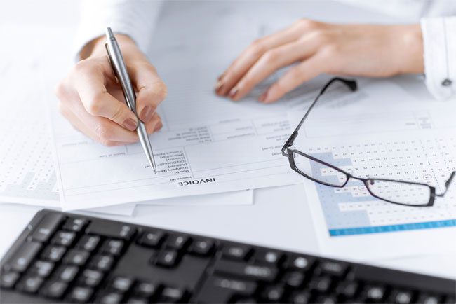 A person reviewing an invoice, with a pen and glasses nearby, representing accounts receivable follow-up