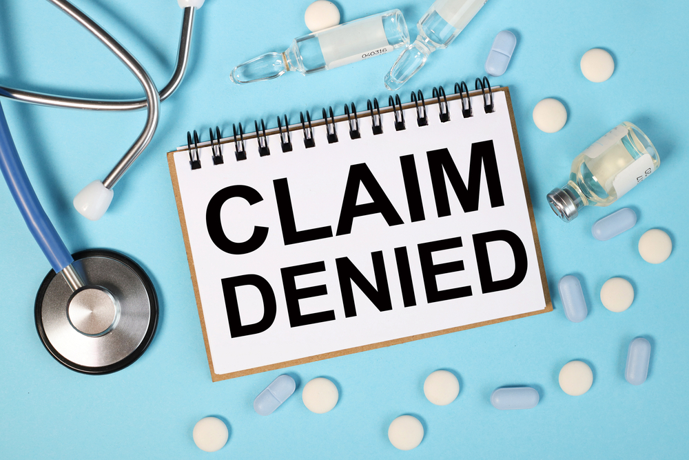 Stethoscope, medicine bottles, and pills with a notebook displaying 'CLAIM DENIED'
