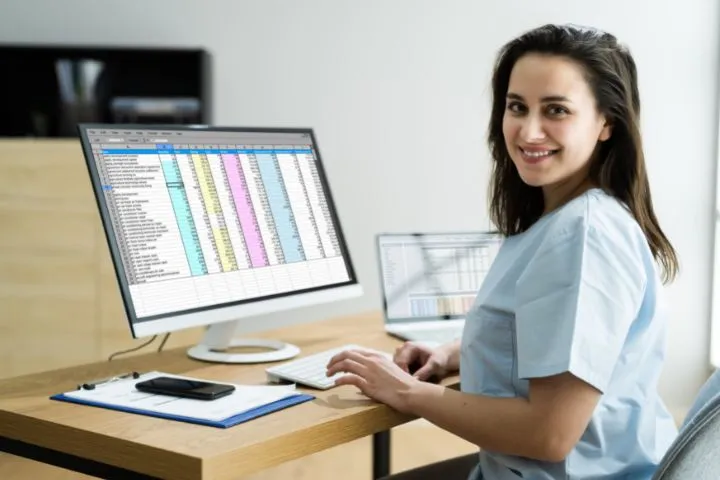 A healthcare professional working on a computer with a spreadsheet, likely handling medical billing or coding tasks.