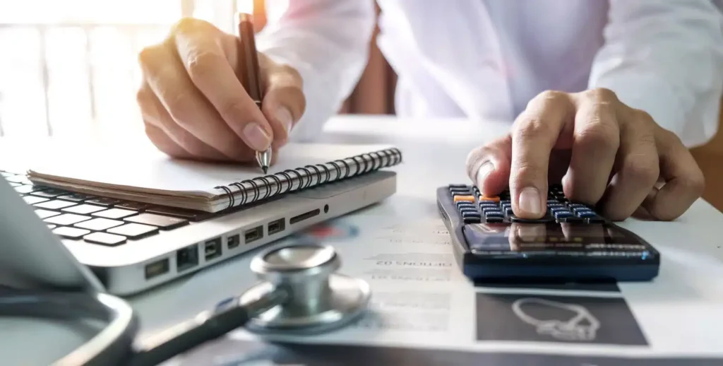A person working on medical billing with a laptop, calculator, and notebook.