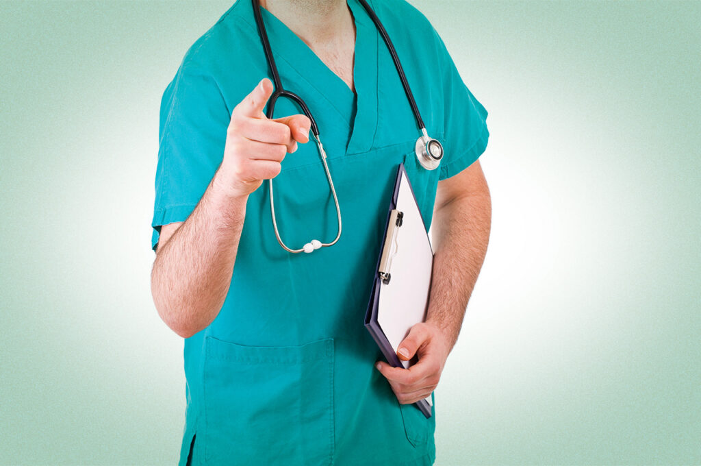 Doctor in scrubs pointing forward while holding a clipboard.