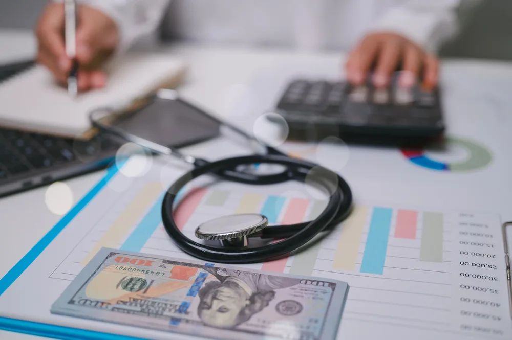 Medical office desk with a stethoscope, money, financial charts, and a calculator