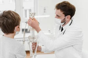 A doctor showing a child a skeletal model while explaining anatomy in a medical office.