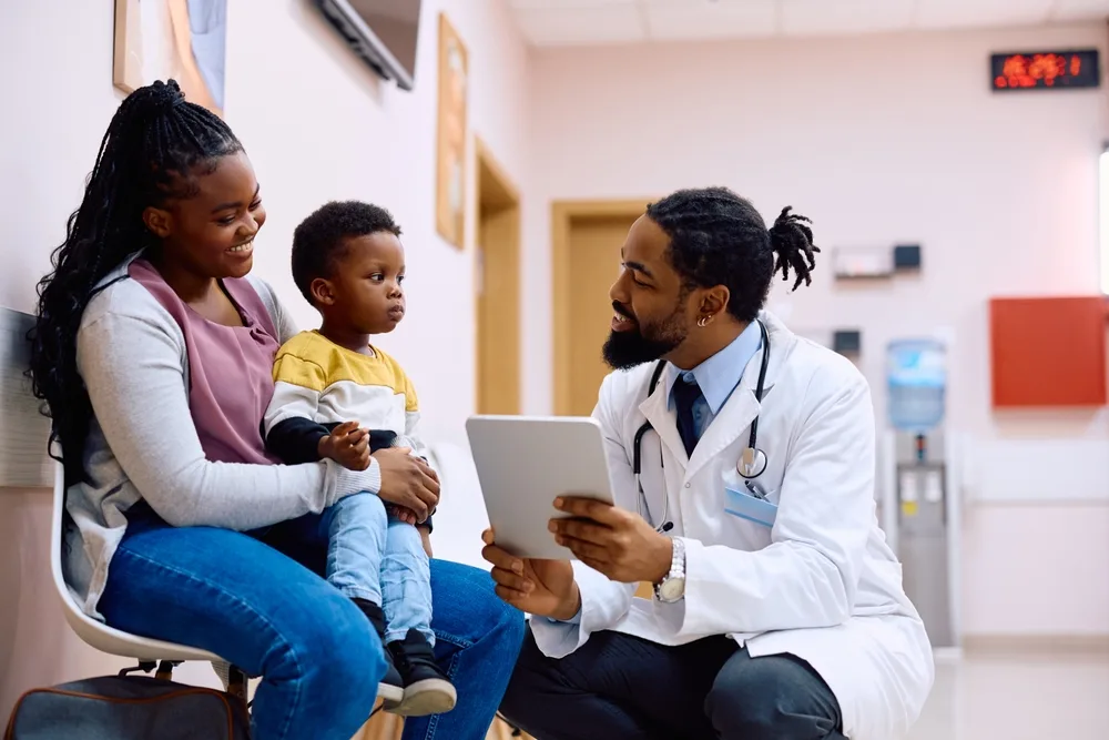 A doctor showing a tablet to a mother and her child during a visit to the clinic.