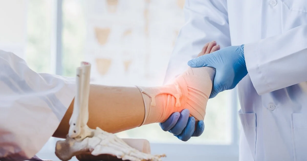 A doctor wrapping a patient's injured ankle with a bandage in a medical setting