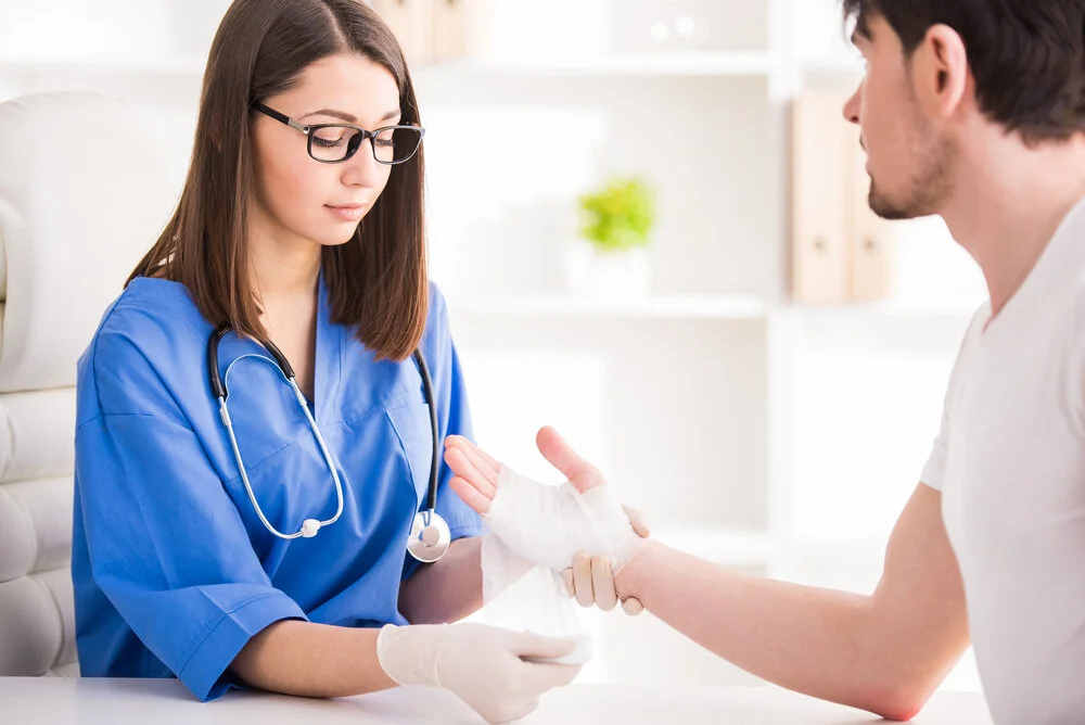 A healthcare professional applying a bandage to a patient's hand in a medical setting