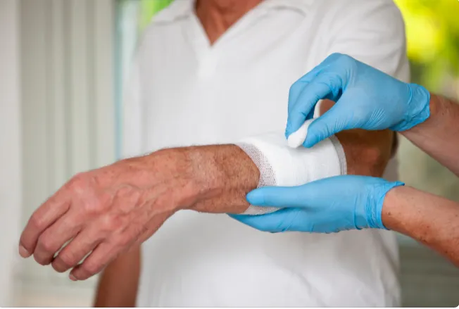 A healthcare professional in blue gloves applying a new dressing to a patient's bandaged arm.
