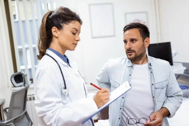 Doctor taking notes while consulting with a male patient in a medical office.