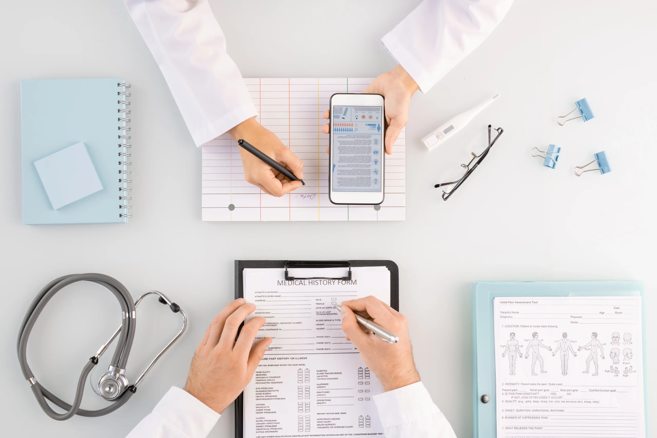 Medical professionals filling out a medical history form, utilizing a smartphone and a stethoscope for patient details.