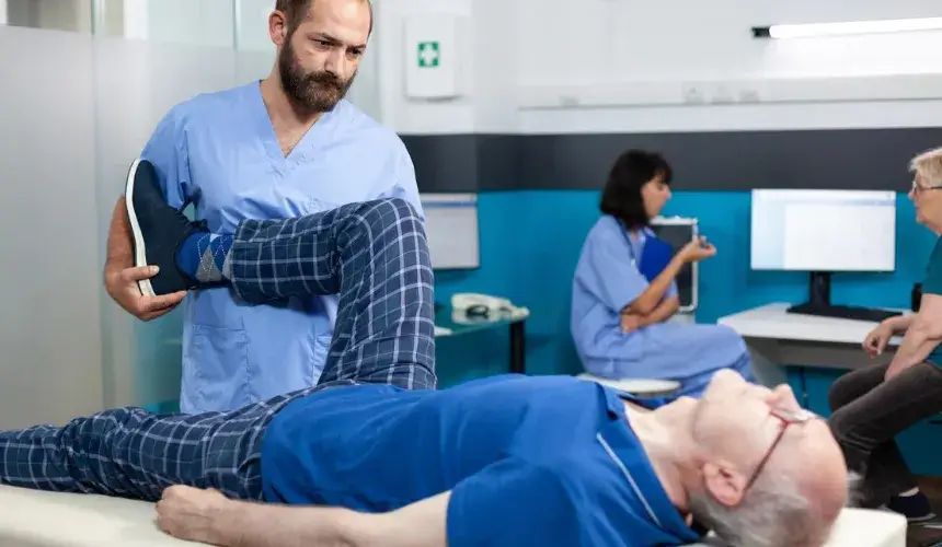 Physical therapist assisting an elderly patient with leg exercises in a rehabilitation setting.