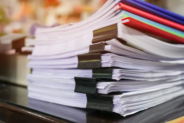 The image shows neatly stacked bundles of paperwork secured with black binder clips.