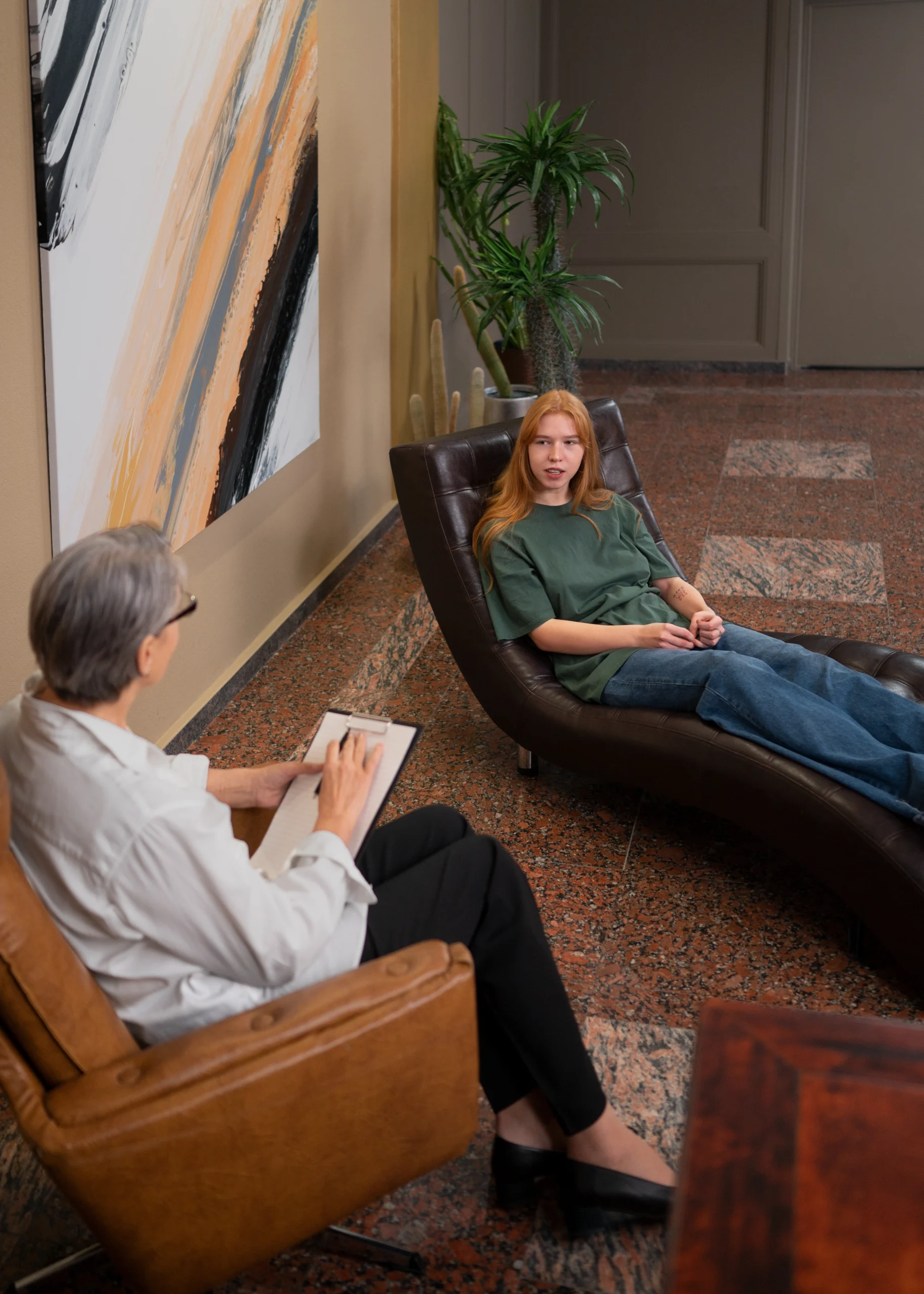 Psychologist taking notes while speaking with a patient during therapy session in office