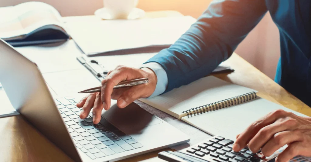 Person using a laptop and taking notes with a pen.