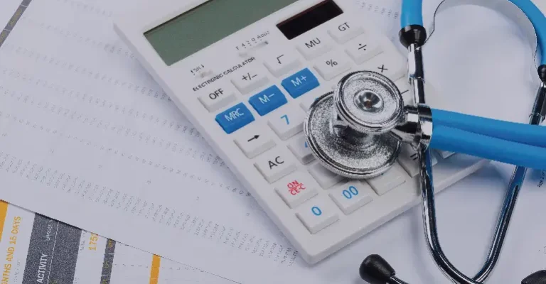 The image shows a calculator next to a stethoscope on a stack of documents, symbolizing healthcare or medical finance.