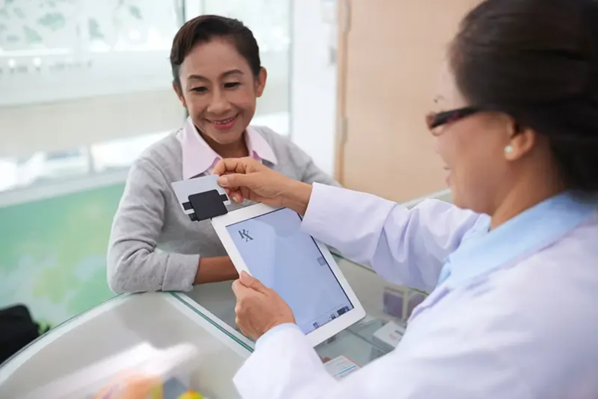 a healthcare professional assisting a patient at a desk, using a tablet to process a card transaction or medical information.